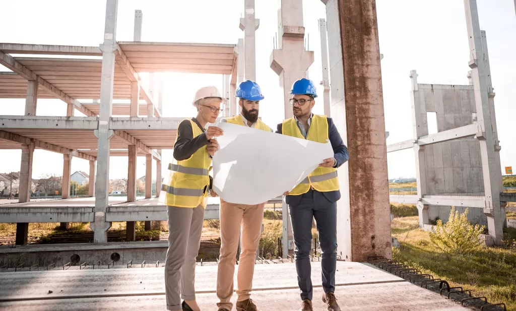 trzy osoby w kaskach i kamizelkach roboczych oglądające plan na placu budowy -  Gewerbe - Jednoosobowa działalność gospodarcza w Niemczech