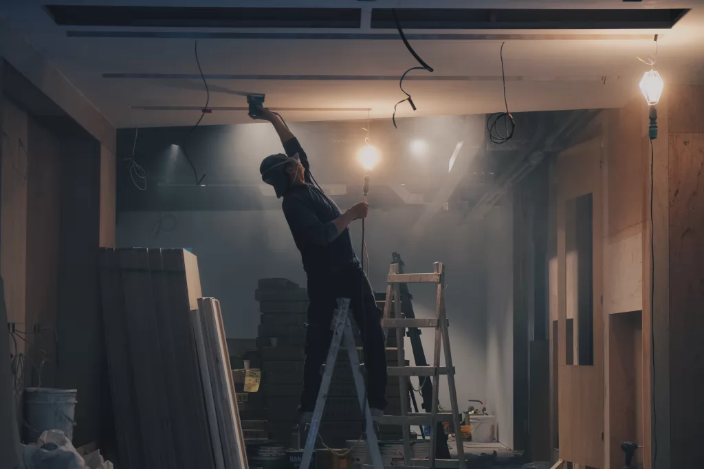 pracownik budowlany maluje sufit stojąc na białej drabinie - ubezpieczenie firmy budowlanej w Niemczech